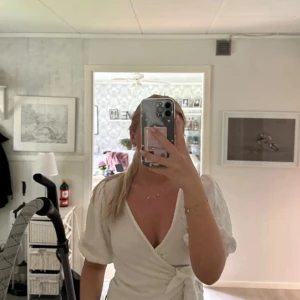 Vit omlottblus från Monki - Säljer en vit omlottblus från Monki med puffiga korta ärmar och knyt framtill. Blusen har en v-ringad design och är gjord i ett lätt, strukturerat tyg som ger en snygg och fräsch look. Perfekt för dig som gillar trendiga och feminina detaljer.