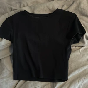 Svart croppad t-shirt topp - En stilren svart croppad t-shirt topp med rund hals och korta ärmar. Enkel och clean design som funkar till många olika looks. Mjuk och skön känsla, perfekt för dig som gillar minimalistisk stil.