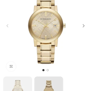 Guldfärgad Burberry klocka - Snygg guldfärgad klocka från Burberry med klassisk rund urtavla och länkarmband i metall. Urtavlan har ett stilrent geometriskt mönster och datumvisning. Perfekt accessoar för dig som gillar exklusiv design och detaljer.