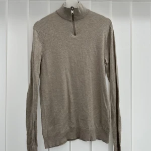 Beige half zip från Jack & Jones - Stilren beige polotröja från Jack & Jones med half zip-dragkedja i halsen. Tröjan är långärmad och har ribbade muddar vid ärmslut och nederkant. Perfekt för lager-på-lager och enkel att matcha med jeans eller chinos.