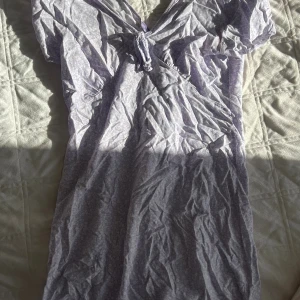 Ljuslila kortklänning från Lefties - Säljer en söt ljuslila kortklänning från Lefties i storlek M. Klänningen har ett diskret blommigt mönster, korta ärmar och v-ringad hals med knyt framtill. Materialet är mjuk bomull, perfekt för varma dagar. Supersnygg och enkel att styla med dina favoritaccessoarer.