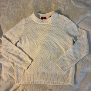 Vit stickad tröja från Esprit - Säljer en vit stickad tröja från Esprit med rund halsringning och diskret strukturmönster. Tröjan har långa ärmar och breda ribbade muddar vid ärmslut och nederkant. Perfekt för lager-på-lager under kyliga dagar. Tröjan är använd 1 gång