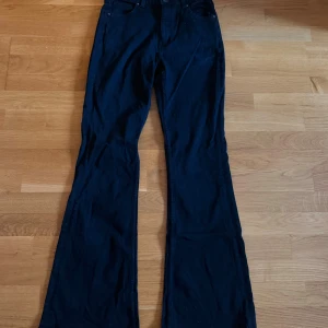 Svarta bootcut jeans från Bershka - Snygga svarta jeans från Bershka i bootcut-modell med hög midja. Klassisk femficksdesign, dragkedja och knapp framtill. Jeansen har en mörk ton och är tillverkade i ett mjukt bomullsmaterial med lite stretch för extra komfort.