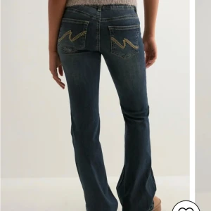 Mörkblå bootcut jeans med broderi - Snygga mörkblå jeans med bootcut passform och coolt gult broderi på bakfickorna. Jeansen har dubbla knappar i midjan och klassiska fickor fram och bak. Perfekta för dig som gillar en tidlös men trendig look. Helt nya med lappen kvar då de va för små. 