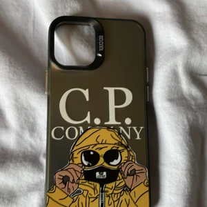 C.P. Company iPhone Skal - Stilrent iPhone-skal med C.P. Company-motiv och illustration. Skalet är genomskinligt med svarta och gula detaljer. Viss yttre slitage och repor syns på baksidan, men knappar och kanter är hela. Passar utmärkt för dig som vill skydda din iPhone med stil. Till iPhone 12 mini