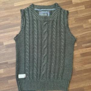 Stickad grå väst - Mysig stickad väst från Race Marine i mörkgrå färg med klassiskt flätmönster. Sparsamt använt. Passar stl S likaväl som M.