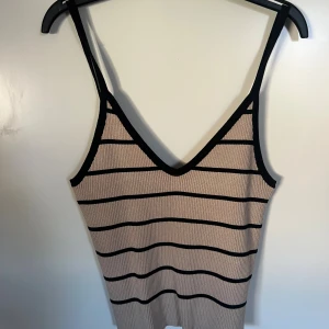Randig ribbad linnetopp från JJXX - Snygg ribbad linnetopp från JJXX i grått med svarta horisontella ränder. Toppen har smala axelband, v-ringning och är figurnära. Perfekt för dig som gillar en enkel men trendig look.