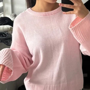 Ljusrosa stickad tröja med vida ärmar - Superfin ljusrosa stickad tröja med breda, ribbade muddar vid ärmslut och nederkant. Tröjan har en loose passform och rund halsringning, perfekt för dig som gillar en chill och söt stil. Materialet är mjukt och känns skönt mot huden.