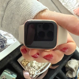 Apple Watch med ljus silikonband - Snygg Apple Watch med fyrkantig svart skärm och ram i roséguld. Klockan har ett stilrent ljus silikonband som är bekvämt att bära hela dagen. Perfekt för dig som gillar tech och vill ha koll på allt direkt på handleden. Nypris 5000kr