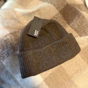 Mörkbrun ribbad mössa  - Snygg mörkbrun ribbad mössa från 157 med uppvikt kant. Perfekt för kalla dagar och enkel att matcha med din höst- eller vinterstil. Materialet är mjukt och värmande, och den neutrala färgen gör den superenkel att bära till allt.