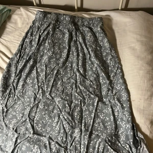 Blommig grå långkjol från 157 Kommer strykt  - Säljer en grå långkjol från 157 med vitt blommigt mönster. Kjolen har resår i midjan för skön passform och är tillverkad i ett mjukt, lätt material som känns luftigt. Perfekt för dig som gillar avslappnad och feminin stil.