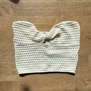 Vit stickad bandeautopp  - Vit/ljusbeige stickad bandeautopp med  knutdetalj framtill. Toppen är från Pull&bear i storlek m men väldigt liten i storleken så passar xs-s.