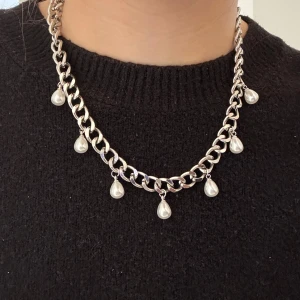 Chunky silverhalsband med pärldroppar - Stilrent halsband med grov silverfärgad kedja och hängande droppformade pärlor. Kedjan har en modern chunky look och pärlorna ger en elegant touch. Perfekt för dig som vill sticka ut med accessoarer som känns både trendiga och klassiska.
