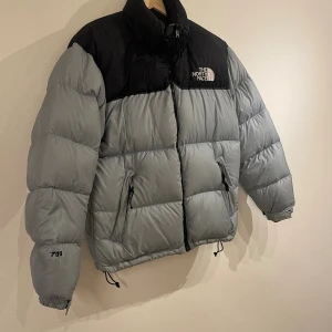 The North Face Nuptse jacka 700 fill - The North Face puffer jacka i häftig ”wolfgrey” grå färg. Finns även en utrullbar luva i nacken. Lättare antydan på användning finns men inget som stör helhetsintrycket och inget som inte borde försvinna i en tvätt.