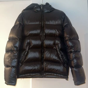 Svart pufferjacka från Zara med huva - Säljer en svart, glansig pufferjacka från Zara med huva och dragkedja framtill. Jackan är S i storlek men passar bra till M också, den är vadderad och har två snedställda fickor. Perfekt för kalla dagar. Hör gärna av dig vid någon fundering 