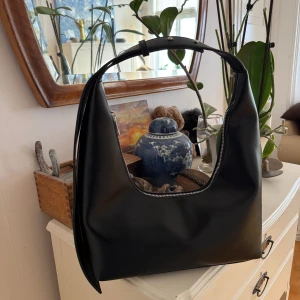 Svart axelväska från NA-KD i skinnimitation - Väska från Nakd. Ny utan prislapp, aldrig använd. Svart. Justerbart handtag mellan 17-28,5 cm. Höjd: 15cm. Bredd 12cm. Längd: 38cm. Stort innerfack med två små fack, ett dragkedja. Silvriga detaljer. Inköpt för 399kr. 