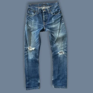 Nudie Jeans grim tim 29/32 - Blå jeans från Nudie Jeans med slitningar och hål på knäna, klassisk femficksmodell och orange sömmar på bakfickorna. Jeansen är i väldigt bra skick. Hålet på bakfickan är design, men kan fixas gratis hos nudie jeans
