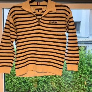 Randig stickad tröja Tommy Hilfiger - Produkten är äkta, köpt på Åhléns i drottning gatan, originals pris 1100kr. Säljer en snygg stickad tröja från Tommy Hilfiger i vitt med svarta ränder. Tröjan har halv dragkedja, krage och broderad Hilfiger-logga på bröstet. Perfekt för dig som gillar klassisk stil med en modern twist.