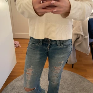 Bootcut ljusblå håliga jeans low waist - Säljer ett par ljusblå jeans med bootcut och låg midja. Jeansen har slitna detaljer och hål på benen för en cool, avslappnad vibe. Regular fit och klassisk femficksmodell. Perfekta för dig som gillar en trendig och bekväm stil.
