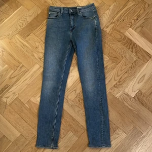 Tiger of Sweden blå jeans Shelly 28/30 - Snygga blå jeans från Tiger of Sweden i modellen Shelly. Klassisk femficksdesign, smal passform och normal midja. Jeansen är i ett mjukt denimtyg och har subtila slitningar för en cool look. Perfekta för dig som gillar stilrena och tidlösa jeans.