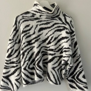 Zebramönstrad stickad polotröja H&M - Säljer en fluffig stickad polotröja från H&M med svartvitt zebramönster. Tröjan har hög krage och är i bra skick då den aldrig kommit till användning.