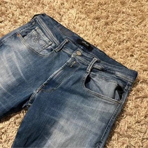  blåa Replay jeans med tvättningar och snygga detaljer - Blå jeans från Replay med tvättningar och snygga kontrastsömmar på bakfickan. Klassisk femficksmodell med Replay-logga på fickan och läderpatch bak i midjan. Jeansen har en slimfit passform och är tillverkade i mjukt denimtyg.