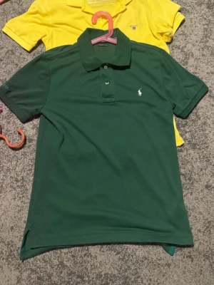 Grön piké från Ralph Lauren - Snygg grön pikétröja från Ralph Lauren med klassisk krage och knappar framtill. Ikoniska loggan broderad på bröstet. Perfekt till jeans eller shorts för en clean look.