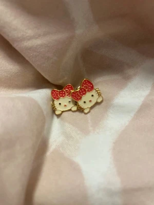 Örhänge  - Bilderna visar inga västar utan ett par Hello Kitty-örhängen i guld och rött. Ingen väst att beskriva.