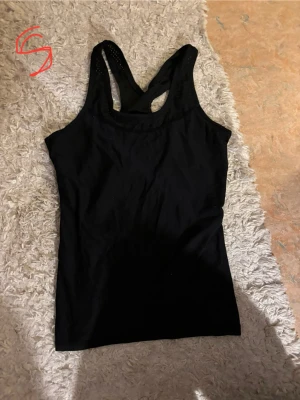 Svart linne - Säljer en enkel och stilren svart linnetopp med brottarrygg. Perfekt till jeans eller shorts och funkar lika bra till träning som till vardags. Materialet känns mjukt och stretchigt för skön passform.