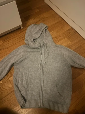 Grå stickad hoodie från Brandy Melville - Mysig grå stickad hoodie från Brandy Melville med dragkedja framtill, huva med snörning och två fickor. Perfekt för lager på lager och chill dagar. Ribbstickade muddar vid ärmslut och nederkant ger en snygg finish. Priset kan diskuteras!