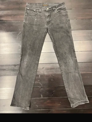 Svarta Nudie Jeans straight fit - Säljer ett par svarta jeans från Nudie Jeans med klassisk femficksmodell och raka ben. Jeansen har slitna detaljer och Nudie-loggan broderad på bakfickorna. 34/34 med stretch och modellen heter slim Jim 