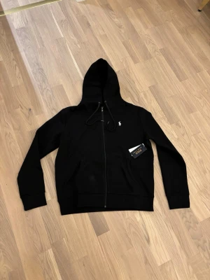 Svart Polo-kofta –  - Svart kofta från Polo i en stilren och tidlös design. Plagget är fått i present men har inte kommit till användning, därför säljs den vidare. Koftan är i fint skick och har en bekväm passform. Enkel att matcha och passar både till vardags och mer uppklädda tillfällen.