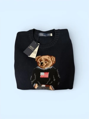 Mörkblå stickad tröja Polo Bear - Mörkblå stickad tröja från Polo Ralph Lauren med ikoniska Polo Bear-motivet framtill. Rund halsringning, ribbade muddar och RL-broderi nertill. Perfekt för dig som vill ha en klassisk men lekfull look.