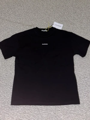 Svart Acne Studios t-shirt - Lite oversized svart t-shirt från Acne Studios med diskret logga broderad på bröstet. Klassisk rund hals och korta ärmar. Tillverkad i mjuk bomull för en clean och stilren look. Perfekt basplagg för alla tillfällen. Skriv om intresse och om du vill ha fler bilder.