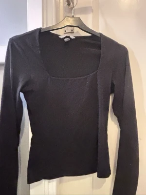 Svart långärmad topp från H&M - En stilren svart långärmad topp från H&M i storlek XS. Toppen har en fyrkantig urringning och är figurnära i modellen. Tillverkad i ett mjukt och stretchigt material som känns bekvämt mot huden. Perfekt att matcha med jeans eller kjol för en clean look.