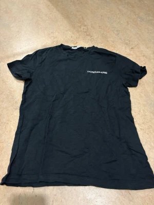 Svart t-shirt från Calvin Klein Jeans - En svart t-shirt från Calvin Klein Jeans med enkel och clean design. T-shirten har korta ärmar och en liten logga tryckt på bröstet. Tillverkad i mjuk bomull som känns skön mot huden. Perfekt till jeans eller shorts.