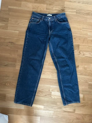Blå raka jeans från Gina Tricot - Säljer ett par klassiska blå jeans från Gina Tricot, modell 'perfect jeans'. Jeansen har rak passform och medelhög midja. Tillverkade i kraftigt denimtyg med snygga kontrastsömmar och läderpatch bak. Perfekta till alla dina outfits!
