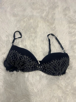 Blå spets-bh från Intimissimi - Snygg mörkblå bh från Intimissimi med tunna axelband och vacker spetsdetalj i vitt över kuporna. Bh:n har en feminin design med broderade blommor och justerbara band för bästa passform.