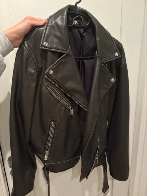 Mörkgrön skinnjacka från Zara - Snygg mörkgrön skinnjacka från Zara. Flera dragkedjor och bälte i midjan. Jackan har långa ärmar och coola detaljer i silver. Aldrig använd.
