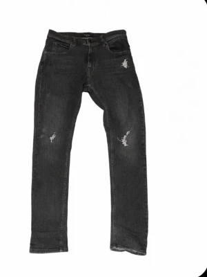 Replay svarta jeans med slitningar - Säljer ett par svarta Replay jeans med snygga sopade slitningar på låren och knäna. Klassisk femficksmodell med raka ben och normal passform. Jeansen har en mörk tvätt och är tillverkade i slitstarkt denimtyg.