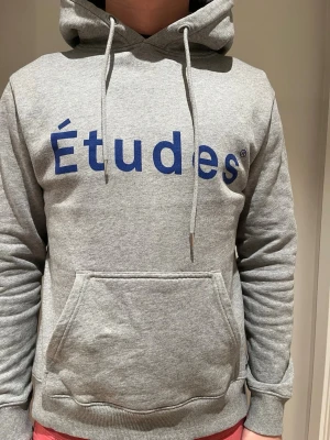 Grå hoodie från Études - 10/10 skick, knappt använd och är i storlek S. Anledning till att jag säljer är att den är liten och tajt för mig. Jag är 185 cm lång och väger 74kg. 