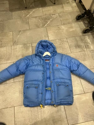 Blå dunjacka från Fjällräven - Blå dunjacka från Fjällräven, Stl S, Dragkedjan är lite trasig, ingen retur. Finns fläckar men går nog bort i tvätten. 