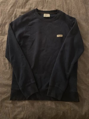 Mörkblå sweatshirt från Nudie Jeans - Mörkblå sweatshirt från Nudie Jeans i 100% ekologisk bomull. Klassisk rund halsringning, ribbade muddar och diskret logga på bröstet. Enkel och stilren design som funkar till allt. Pris kan diskuteras