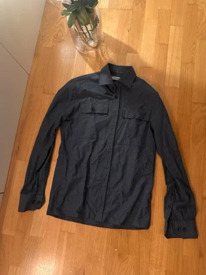 Mörkblå skjorta från Lagency - Snygg mörkblå skjorta från Lagency med klassisk krage och två bröstfickor med knappar. Skjortan har långa ärmar med manschetter och knappar, perfekt för en clean och stilren look. Materialet känns mjukt och är troligtvis bomull.