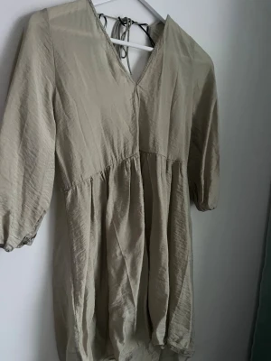 Sommarklänning H&M - Luftig olivgrön grön kortklänning från H&M i storlek XS. Klänningen har v-ringning både fram och bak med knytband i nacken, samt trekvartsärmar med lätt puff. Använd fåtal gånger, bra skick💚