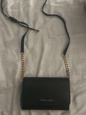 Svart axelväska från Michael Kors - Snygg svart axelväska från Michael Kors i skinn med guldfärgade kedjedetaljer och logga framtill. Passar med allt!!💕💕 