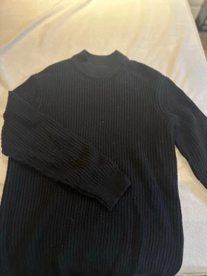 Svart ribbad stickad tröja Brave Soul - Säljer en svart ribbad stickad tröja från Brave Soul i storlek L. Tröjan har hög hals och långa ärmar, perfekt för kyligare dagar. Enkel och stilren design som funkar till det mesta. Materialet är mjukt och ger en skön känsla.