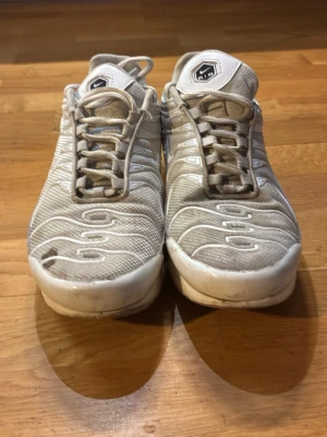 Nike Air Max vita sneakers - Nike Air Max sneakers i vitt med mesh och syntetpaneler, ikoniska vågiga detaljer på ovandelen och synlig Air-enhet i sulan. Skorna har snörning och en chunky, sportig vibe som passar perfekt till streetwear. Swoosh-logga på sidan och AIR-märke på plösen.