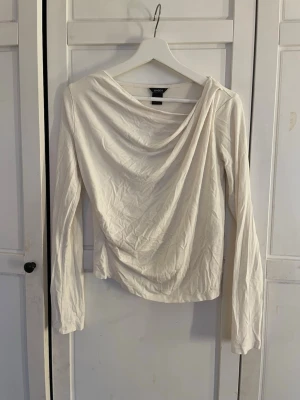 Vit omlottopp från Lindex - Säljer en vit omlottopp från Lindex i storlek S. Toppen har långa ärmar och en snygg draperad omlottdesign framtill. 