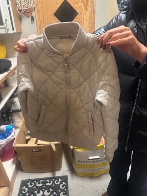 Beige quiltad bomberjacka Rosetti - Säljer en beige quiltad bomberjacka från Rosetti i storlek 134/140. Jackan har ribbad krage, dragkedja framtill och två fickor. Perfekt för dig som gillar stilren och enkel design med en sportig touch.